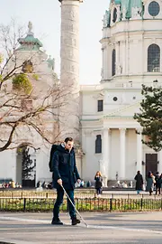 Blind person walks with a cane along the guidance system for the blind in front of St. Charles Church in Vienna